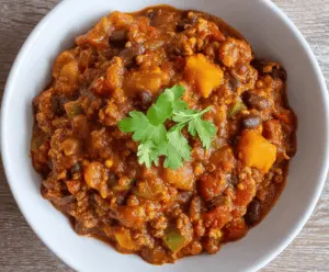 A bowl of hearty pumpkin chili topped with shredded cheese and fresh herbs, served with bread on the side—perfect for cozy fall meals.