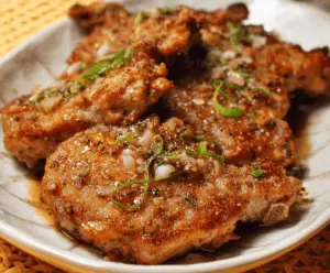 Juicy salt and pepper seasoned pork chops garnished with fresh herbs on a rustic wooden cutting board
