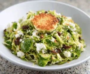 Crispy Brussels sprout salad topped with creamy goat cheese and crunchy nuts, served in a bowl.