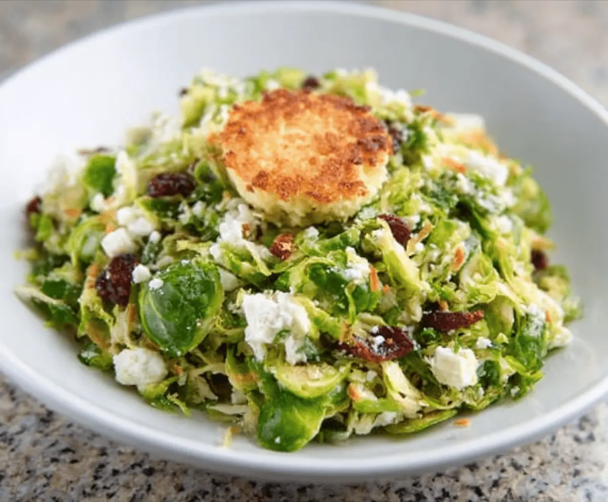 Crispy Brussels sprout salad topped with creamy goat cheese and crunchy nuts, served in a bowl.