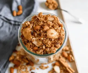 Homemade vanilla almond granola in a glass jar with fresh almonds and vanilla beans.