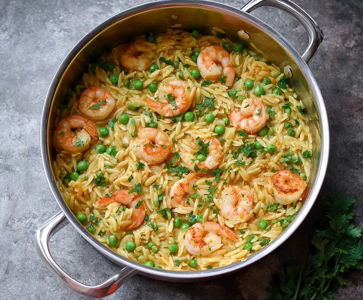 Delicious one-pot pea and shrimp orzo pasta dish garnished with fresh herbs.