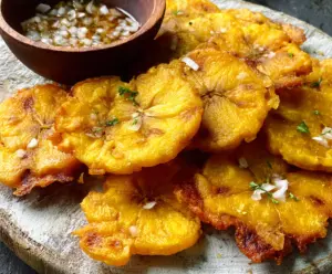 Crispy golden tostones topped with fresh herbs on a rustic wooden plate