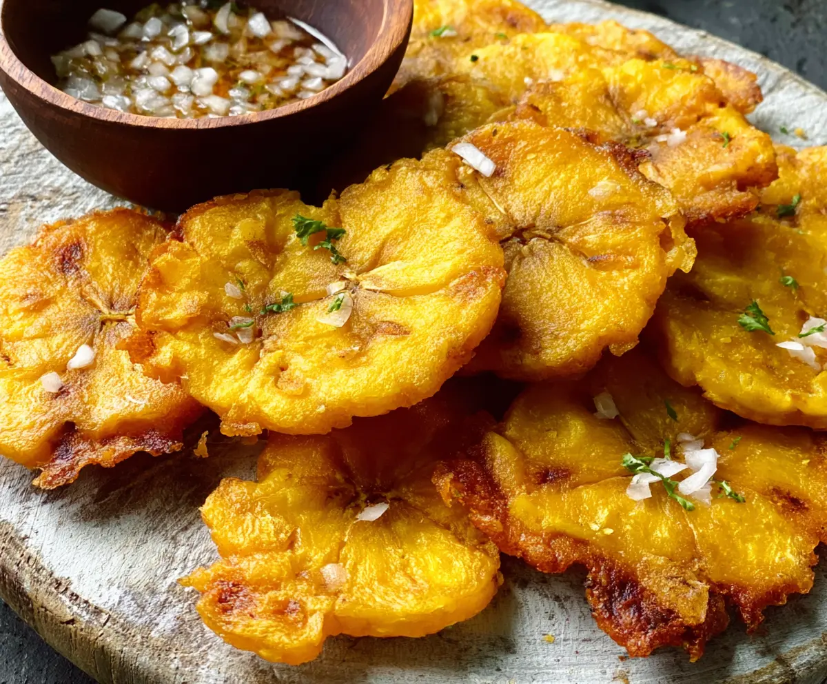 Crispy golden tostones topped with fresh herbs on a rustic wooden plate